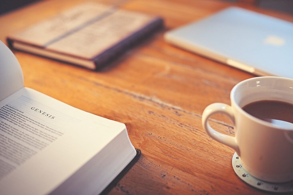 Table with Bible, journal, computer, and coffee.