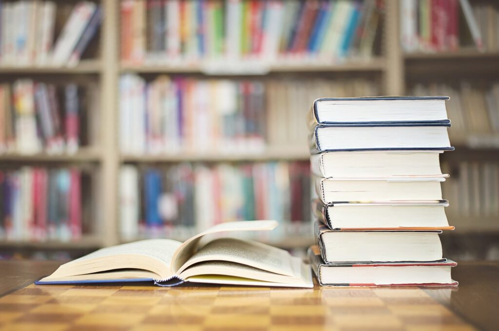 Stacks of books on a table with bookshelves behind it.